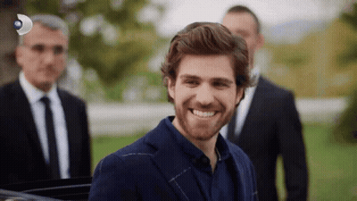 A Man In A Suit And Tie Is Smiling In Front Of A Group Of Men In Suits GIF