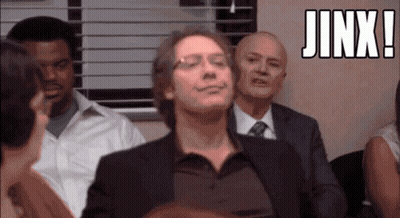 A Man In A Suit And Tie Is Smiling In Front Of A Group Of People And The Word Jinx Is Above Him GIF