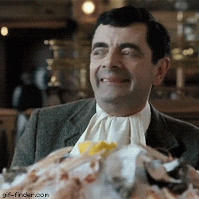 A Man In A Suit And Tie Is Smiling In Front Of A Pile Of Food With Gif-Finder.com In The Corner GIF