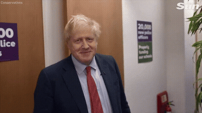 A Man In A Suit And Tie Is Smiling In Front Of A Sign That Says Conservatives On It GIF