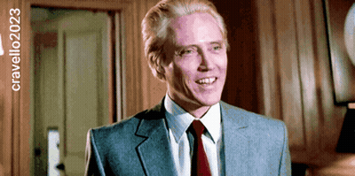 A Man In A Suit And Tie Is Smiling In Front Of A Sign That Says Cravello2023 GIF