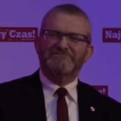 A Man In A Suit And Tie Is Smiling In Front Of A Sign That Says " Czas " GIF