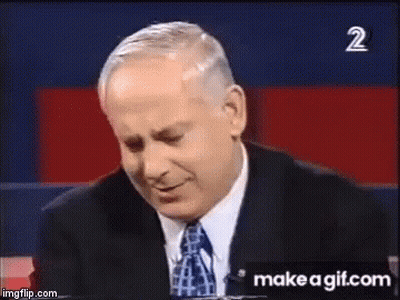 A Man In A Suit And Tie Is Smiling In Front Of A Sign That Says Make A Gif.com . GIF