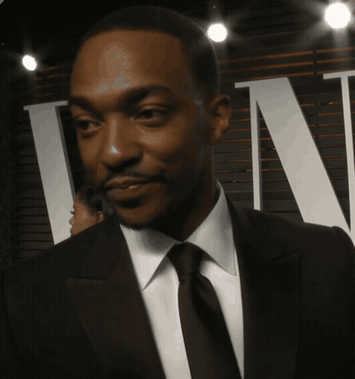 A Man In A Suit And Tie Is Smiling In Front Of A Sign That Says Tn GIF
