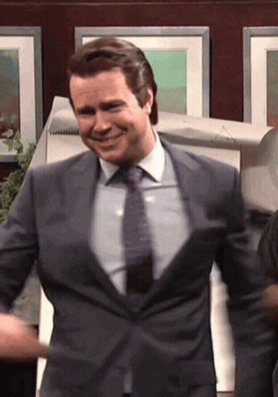 A Man In A Suit And Tie Is Smiling In Front Of A Wall Of Pictures GIF