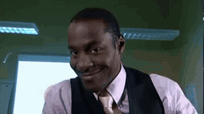 A Man In A Suit And Tie Is Smiling In Front Of A Window . GIF