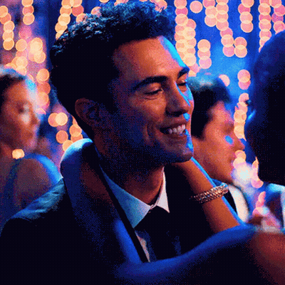 A Man In A Suit And Tie Is Smiling While Holding A Woman 'S Arm GIF