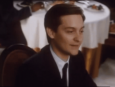 A Man In A Suit And Tie Is Smiling While Sitting At A Table . GIF