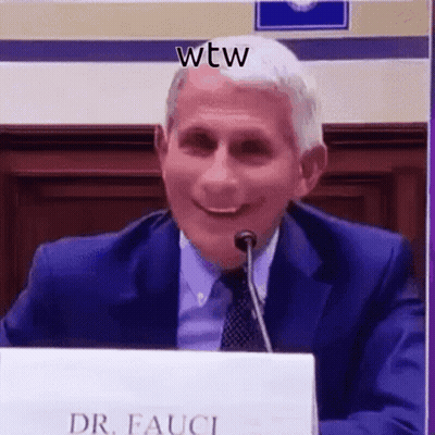 A Man In A Suit And Tie Is Smiling While Sitting At A Table With A Microphone . GIF