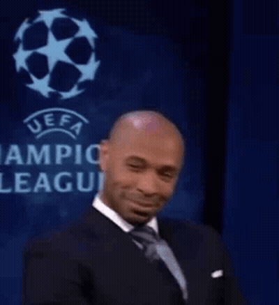 A Man In A Suit And Tie Is Smiling While Sitting In Front Of A Sign That Says Uefa Champions League . GIF
