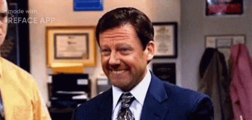 A Man In A Suit And Tie Is Smiling While Standing In A Room . GIF