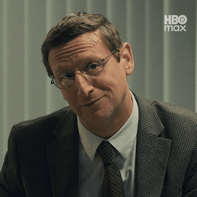 A Man In A Suit And Tie Is Smiling With A Hbo Max Logo In The Background GIF