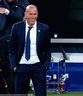A Man In A Suit And Tie Is Smiling With His Hands In His Pockets .. GIF