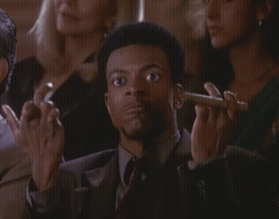 A Man In A Suit And Tie Is Smoking A Cigar In A Crowd Of People GIF