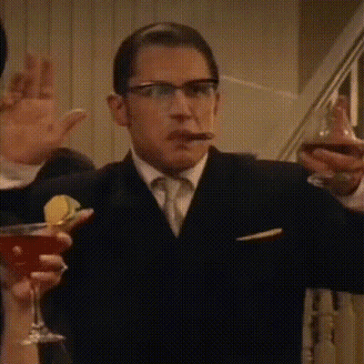 A Man In A Suit And Tie Is Smoking A Cigar While Holding A Martini Glass . GIF