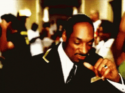 A Man In A Suit And Tie Is Smoking A Cigarette In Front Of A Crowd GIF