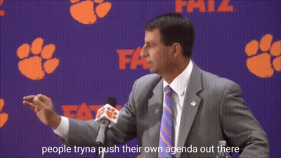 A Man In A Suit And Tie Is Speaking Into A Microphone In Front Of A Clemson Banner GIF