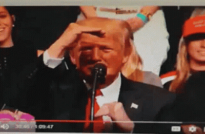 A Man In A Suit And Tie Is Speaking Into A Microphone In Front Of A Crowd GIF
