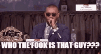 A Man In A Suit And Tie Is Speaking Into A Microphone While Sitting At A Table . GIF