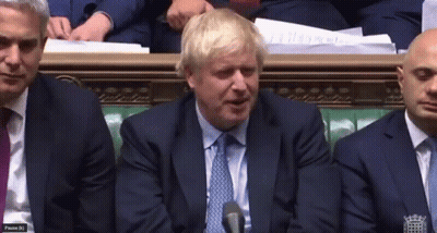 A Man In A Suit And Tie Is Speaking Into A Microphone While Sitting In A Room With Other Men GIF