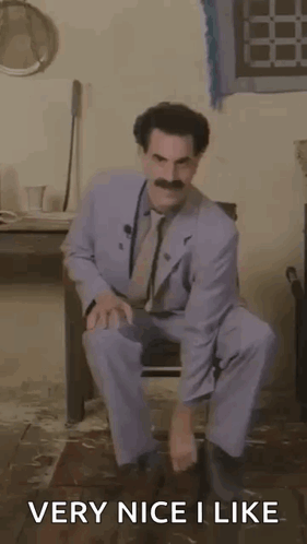 A Man In A Suit And Tie Is Squatting Down In A Room With The Words `` Very Nice I Like '' . GIF