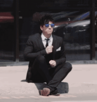 A Man In A Suit And Tie Is Squatting Down On The Ground GIF