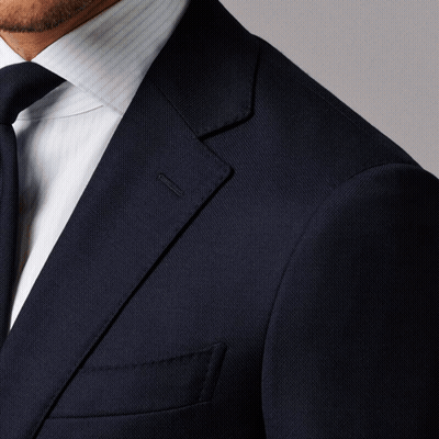 A Man In A Suit And Tie Is Standing Against A Grey Background GIF