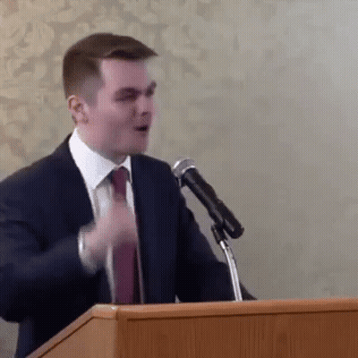 A Man In A Suit And Tie Is Standing At A Podium Giving A Speech In Front Of A Microphone . GIF