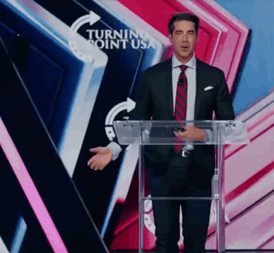 A Man In A Suit And Tie Is Standing At A Podium In Front Of A Turning Point Usa Sign GIF