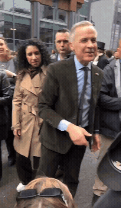 A Man In A Suit And Tie Is Standing In A Crowd Of People GIF