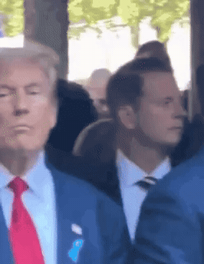 A Man In A Suit And Tie Is Standing In A Crowd Of People GIF