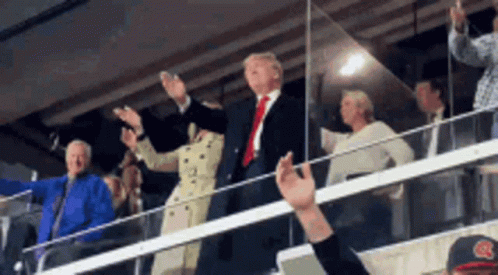 A Man In A Suit And Tie Is Standing In A Crowd With His Arms In The Air GIF