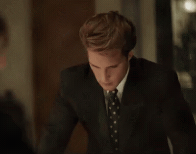 A Man In A Suit And Tie Is Standing In A Dark Room . GIF