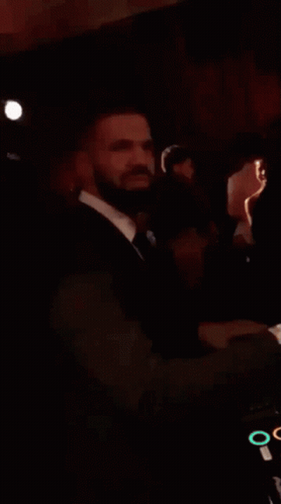 A Man In A Suit And Tie Is Standing In A Dark Room And Smiling . GIF