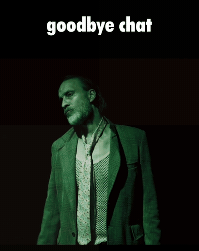 A Man In A Suit And Tie Is Standing In A Dark Room Under A Goodbye Chat Sign GIF