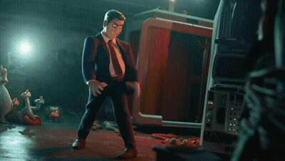 A Man In A Suit And Tie Is Standing In A Dark Room With A Tv In The Background GIF