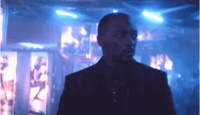 A Man In A Suit And Tie Is Standing In A Dark Room With Blue Lights GIF