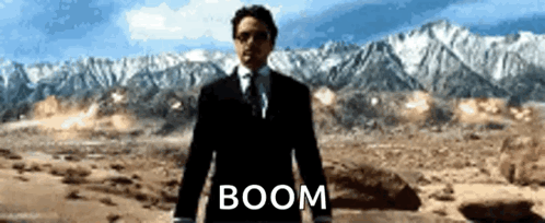 A Man In A Suit And Tie Is Standing In A Desert With The Word Boom Written On The Ground GIF