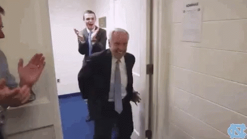 A Man In A Suit And Tie Is Standing In A Doorway While Another Man Applauds . GIF