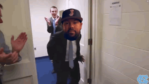 A Man In A Suit And Tie Is Standing In A Doorway With A Schedule On The Wall GIF