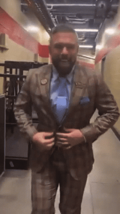 A Man In A Suit And Tie Is Standing In A Hallway Adjusting His Jacket GIF
