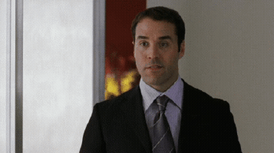 A Man In A Suit And Tie Is Standing In A Hallway GIF