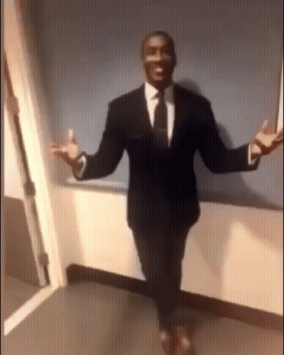 A Man In A Suit And Tie Is Standing In A Hallway . GIF