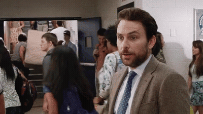 A Man In A Suit And Tie Is Standing In A Hallway Surrounded By Students . GIF