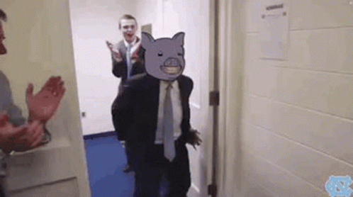 A Man In A Suit And Tie Is Standing In A Hallway With A Cartoon Pig On His Face . GIF