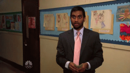A Man In A Suit And Tie Is Standing In A Hallway With A Nbc Logo On The Wall GIF