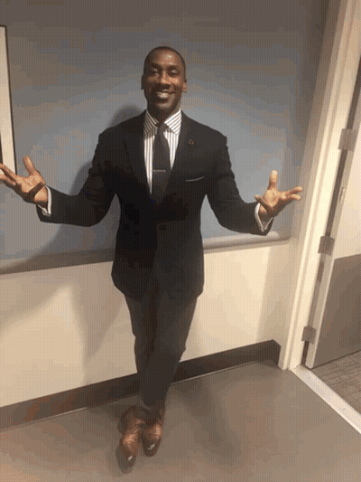A Man In A Suit And Tie Is Standing In A Hallway With His Arms Outstretched GIF