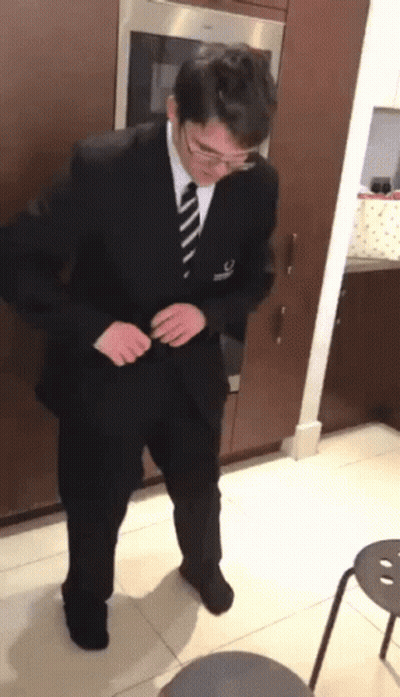 A Man In A Suit And Tie Is Standing In A Kitchen Adjusting His Jacket GIF