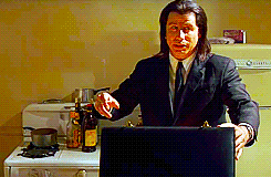 A Man In A Suit And Tie Is Standing In A Kitchen Holding A Laptop GIF