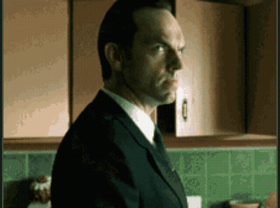 A Man In A Suit And Tie Is Standing In A Kitchen With Green Tiles GIF